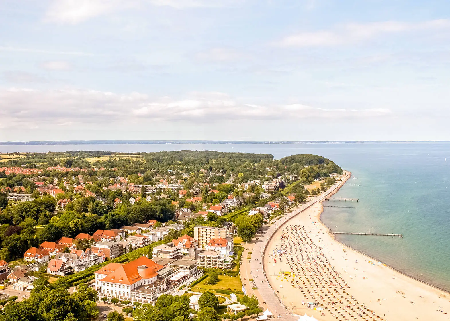 Blick von oben auf einen Küstenabschnitt mit Strand und bewohntem Gebiet mit viel Grün.