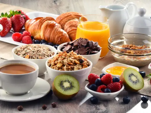 Frühstück mit Croissants, Müsli, Obst, Orangensaft und Kaffee.