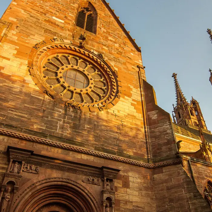 Basler Münster von unten, welches durch die Abendsonne golden scheint.