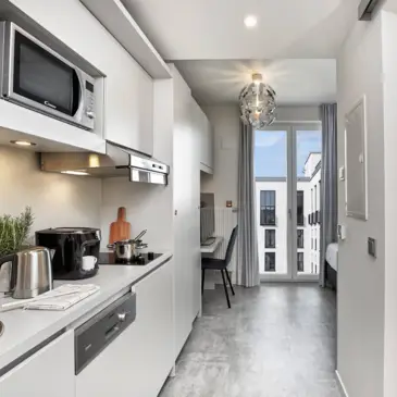 Blick auf ein Apartment mit einer kleinen, vollfunktionstüchtigen Einbauküche auf der linken Seite.