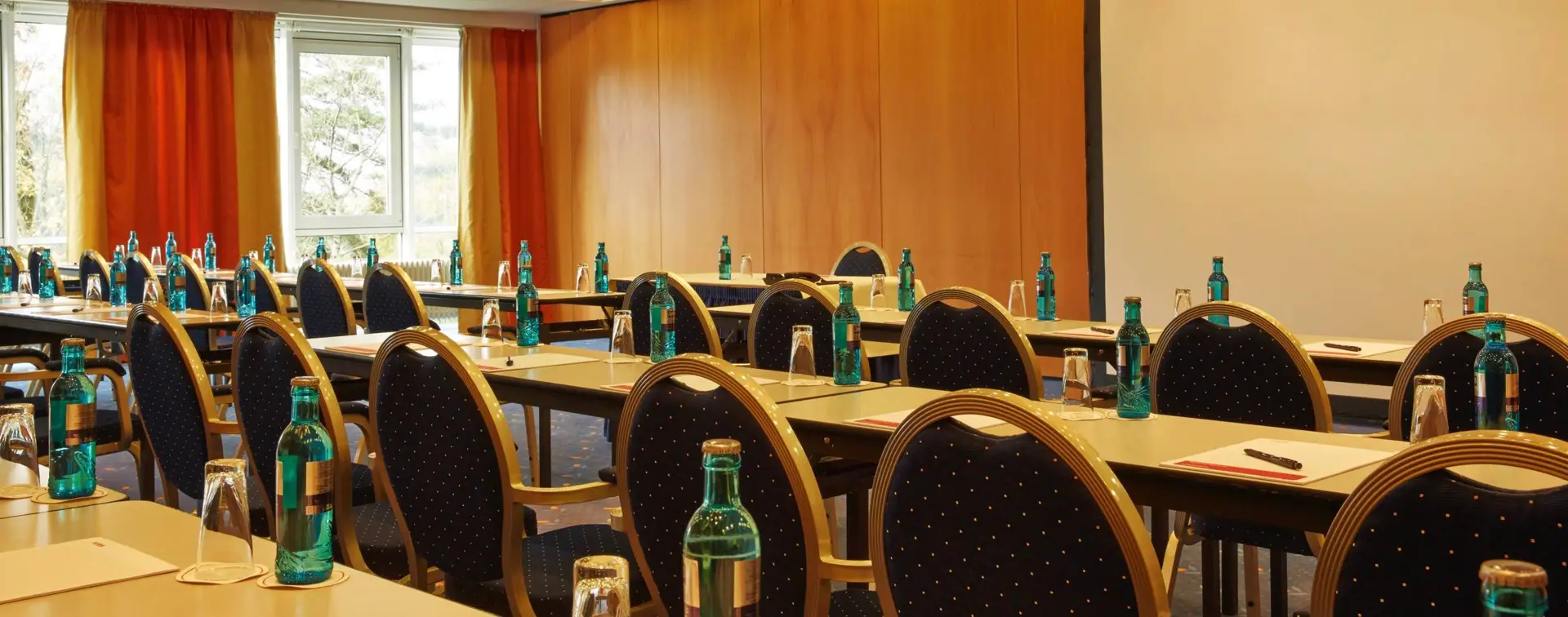 Tagungsraum mit Konferenzbestuhlung. An der Wand hängt eine große Leinwand.