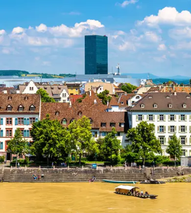 Blick auf Basel über den gelben Rhein. Im Hintergrund ragt das HYPERION Hotel Basel über die Häuser.