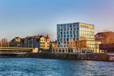 Blick über die Aare auf das Hotel im Herbst. Das Hotel hat eine Würfelform.