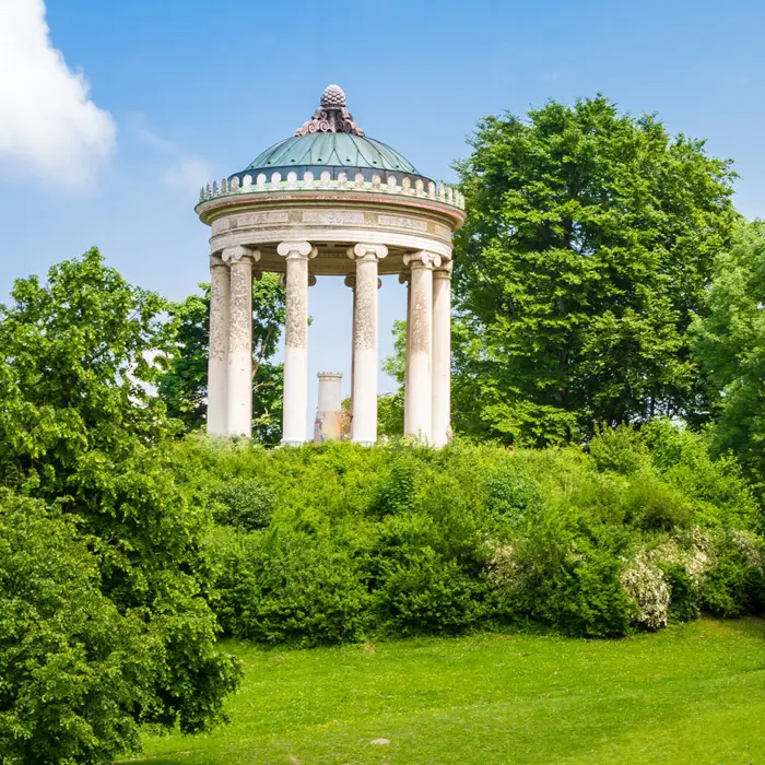 Garten mit Büschen und Rasen. Im Hintergrund steht ein griechisch aussehender Pavilion