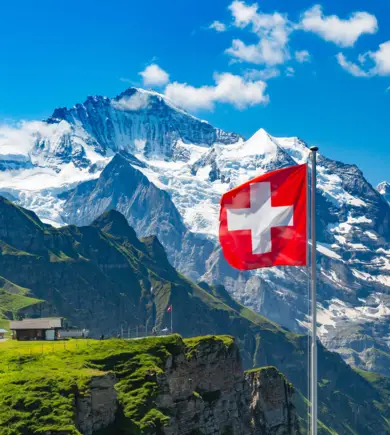 Schweizer Flagge weht im Wind. Im Hintergund ist die Zugspitze mit Schnee.