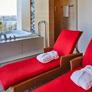 Rote Liegen und ein Whirlpool im Ruhebereich vor einem großen Fenster mit Blick auf die Aare.