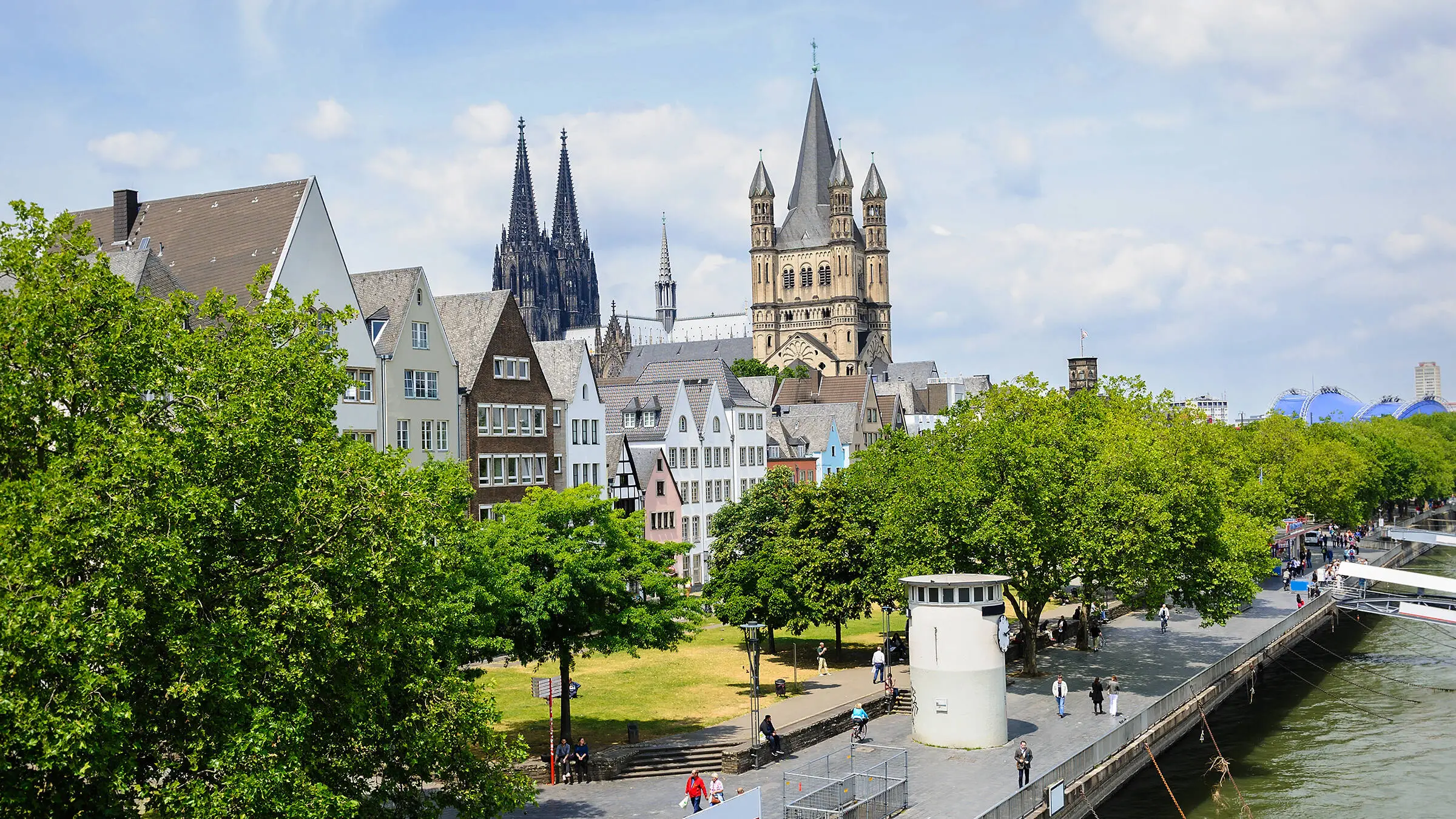 Blick auf die Altstadt und die Rheinuferpromenade in Köln von einer Rheinbrücke aus. Im Hintergrund befinden sich die Türme des Kölner Doms.