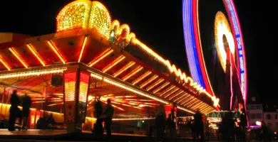 Beleuchteter Autoscouter und daneben ein beleuchtetes Riesenrad bei Nacht.