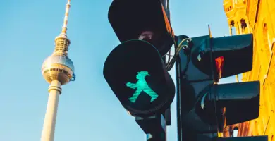 Detailaufnahme einer Ampel mit grünem Ampelmann. Im Hintergrund steht der Fernsehturm.