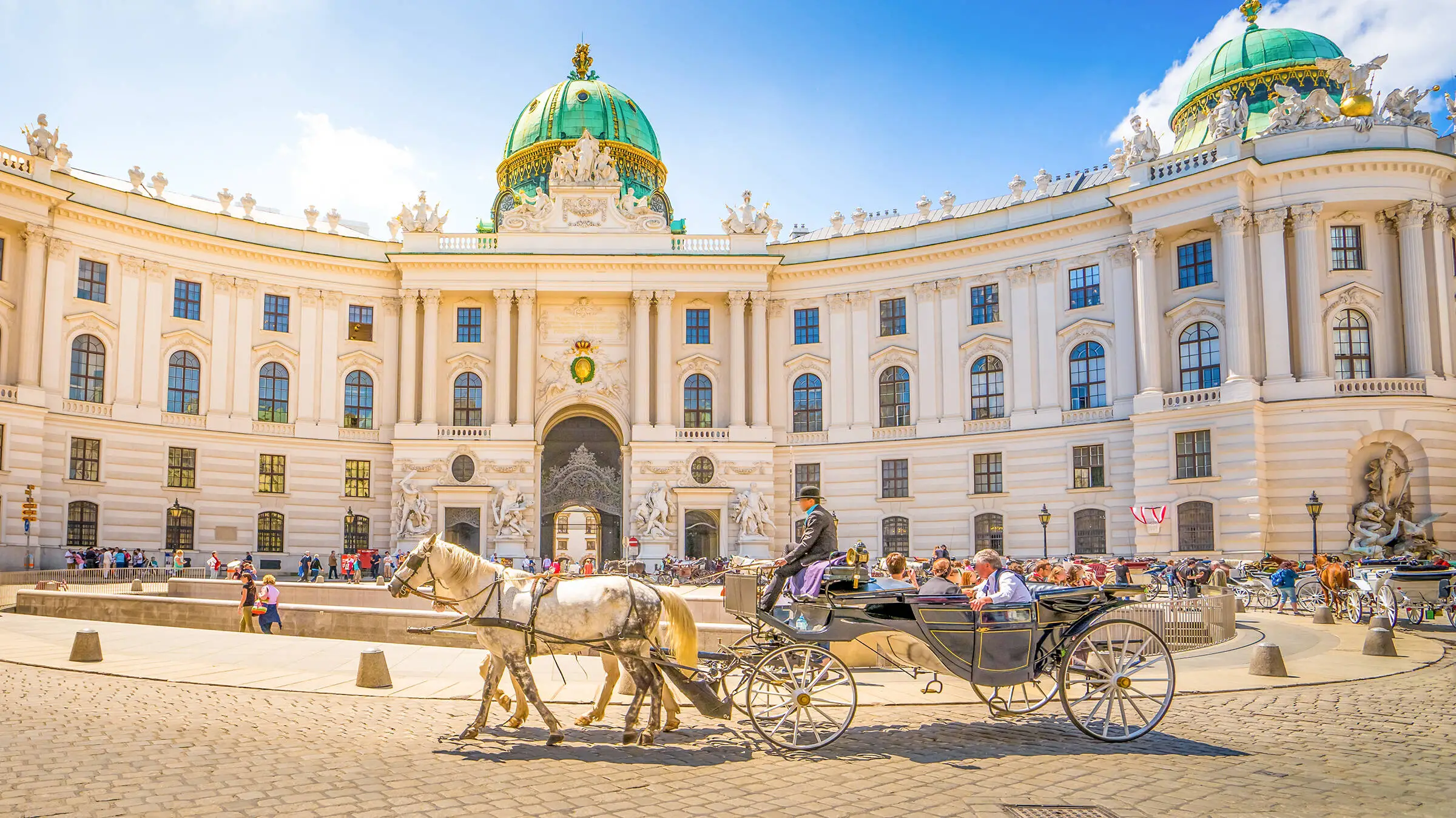 View of the Hofburg Palace in Vienna in the sunshine with a horse-drawn carriage in the foreground.