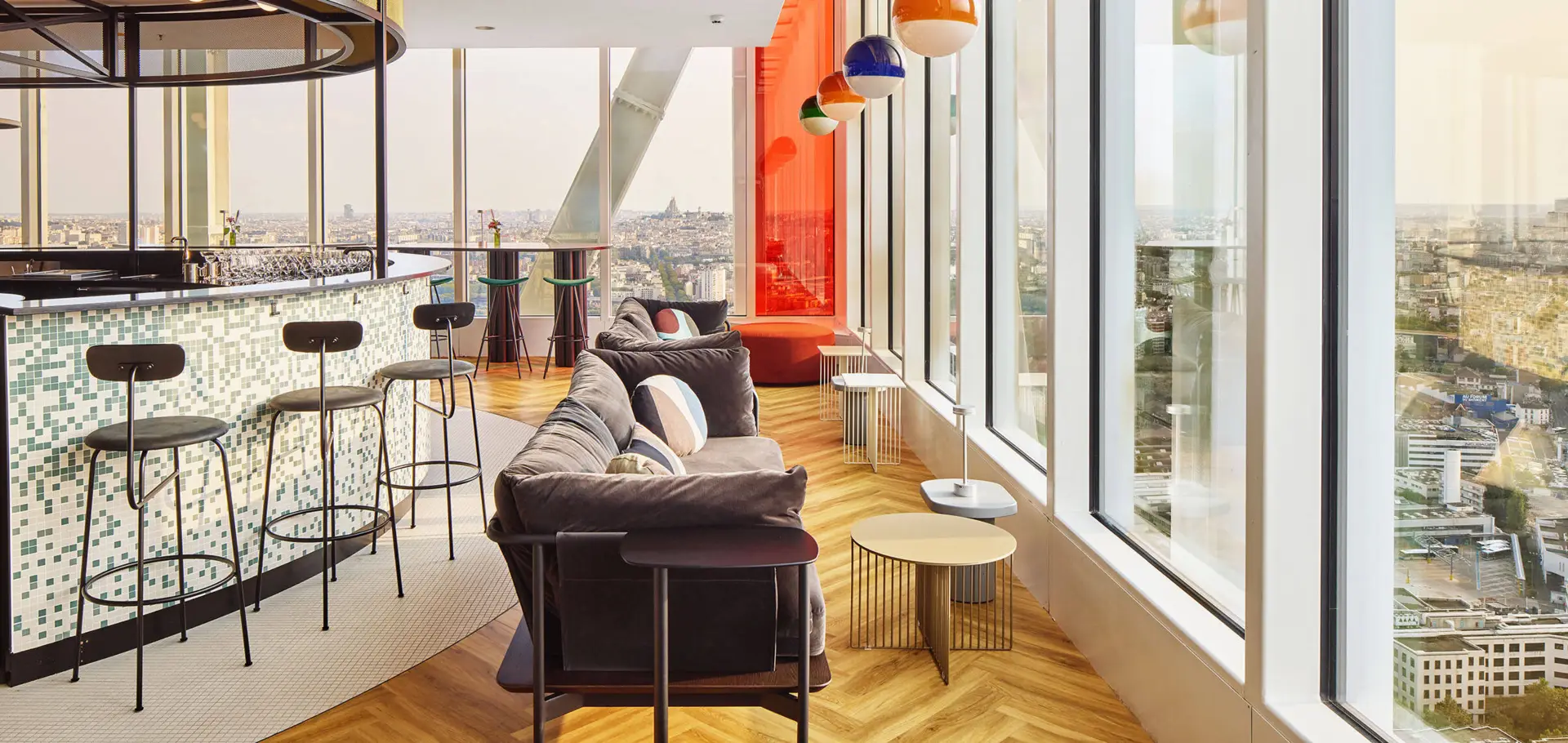 Bar with counter, bar stools and sofa in front of large windows overlooking Paris.