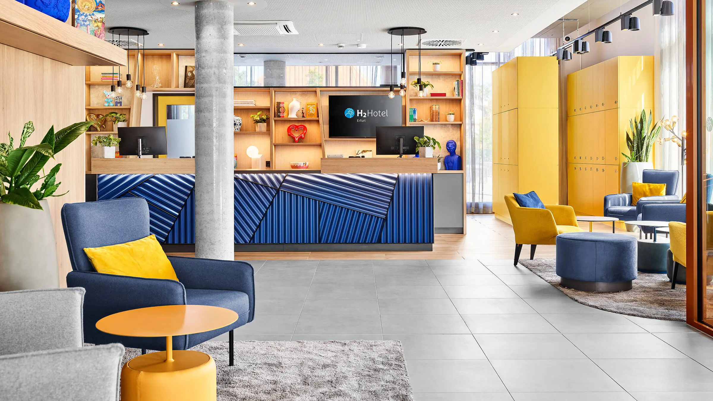 Helle Lobby mit Rezeption und Sesseln mit Tischen.