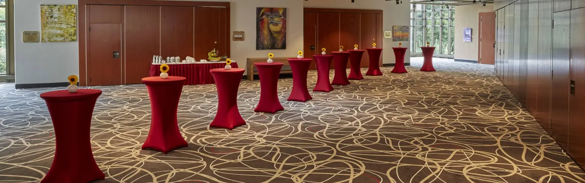 Tagungsfoyer mit vielen Stehtischen in roten Tischhussen. Im Hintergrund steht ein kleines Buffet.