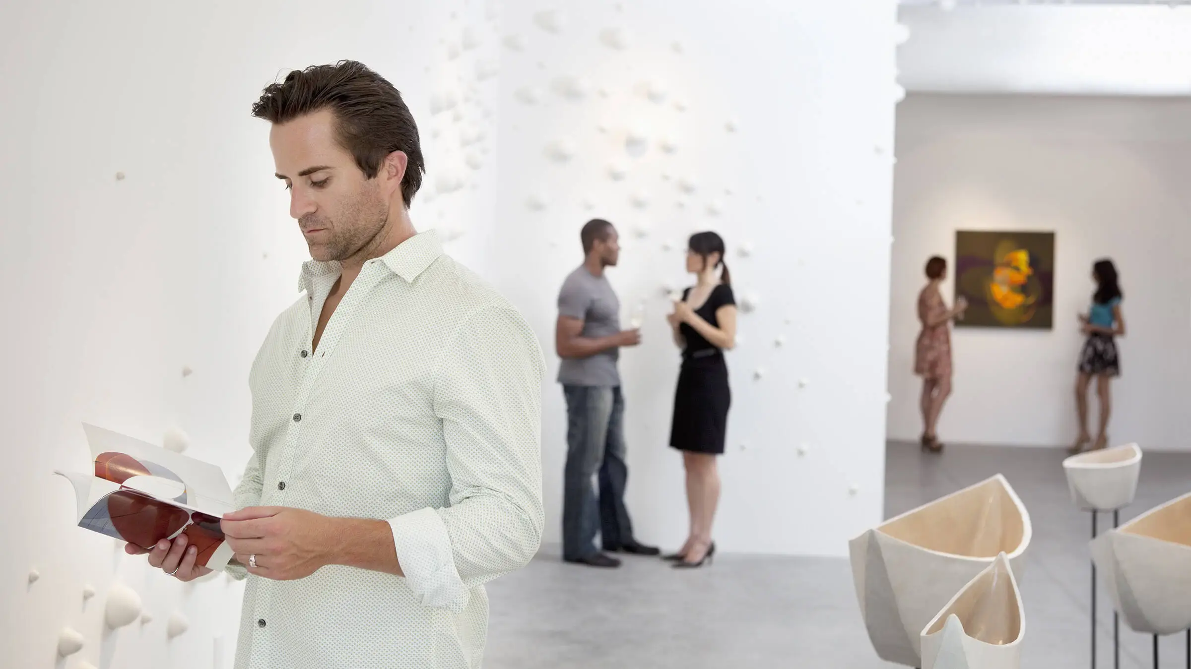 A man in a white shirt looks at a brochure in the museum and stands in front of a sculpture