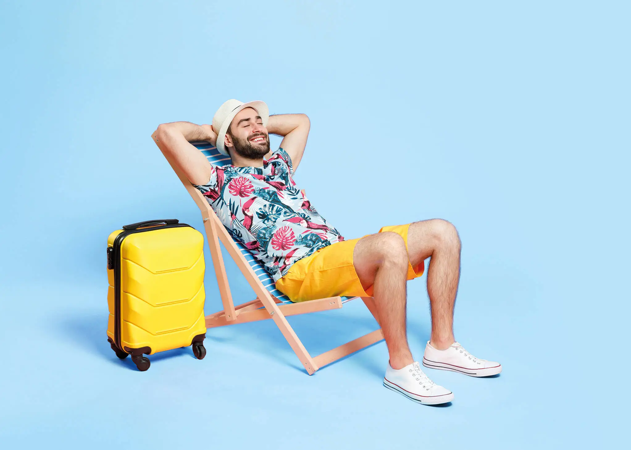 Mann im Sommeroutfit liegt auf einem Liegestuhl vor einem blauen Hintergrund. 