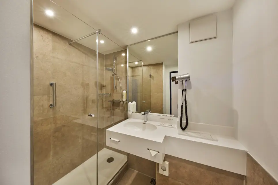 Badezimmer mit einer großen Dusche. Neben der Dusche hängt ein Waschbecken.