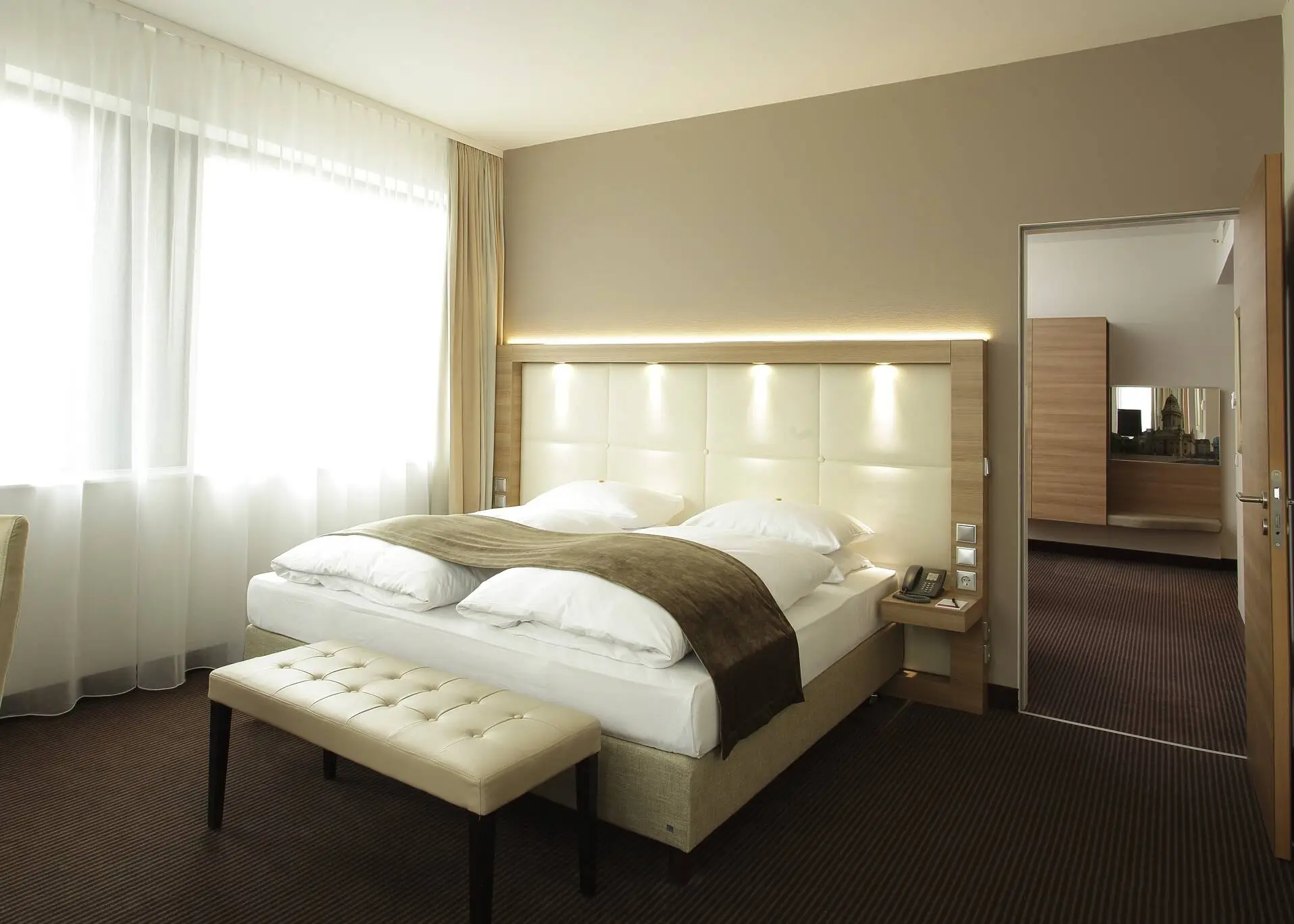 Hotelzimmer in beigegoldenen Farben. In der Mitte des Zimemrs steht ein Doppelbett.