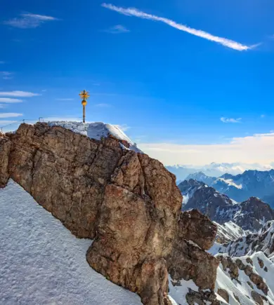 Ein goldenes Gipfelkreuz auf der Zugspitze. Im Hintergrund verläufte die Bergkette.