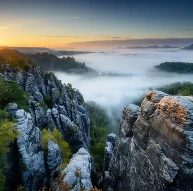 Blick von oben auf ein Felsformation in der sächsische Schweiz. IM Wald hängen Nebelwolken.