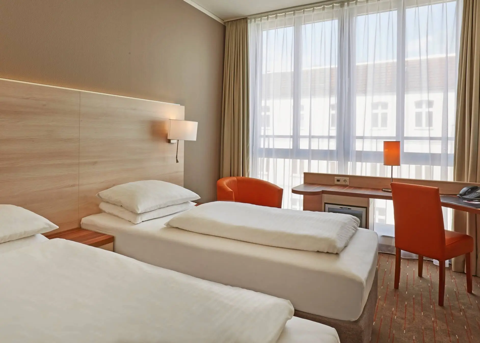 Twin beds in the hotel room. There is a desk in front of the window.