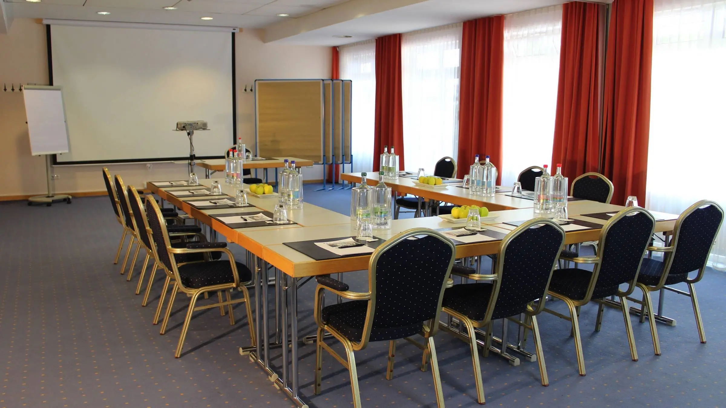 Konferenzraum mit einer UForm Bestuhlung. Hinter dem Rednertisch steht eine große Leinwand und eine Flipchart.