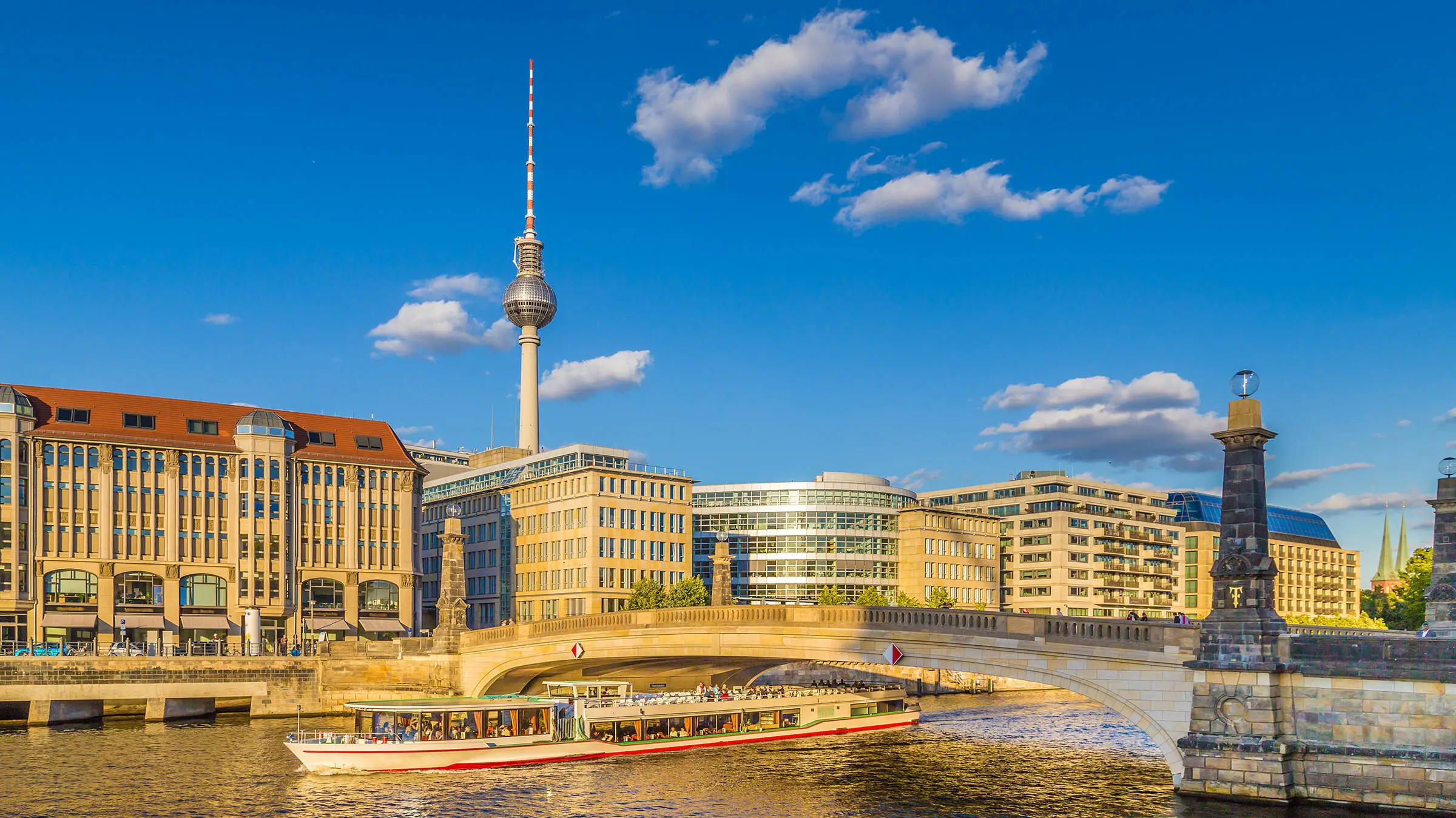 View across the River Spree to Berlin's television tower. An excursion boat passes under a bridge on the Spree.