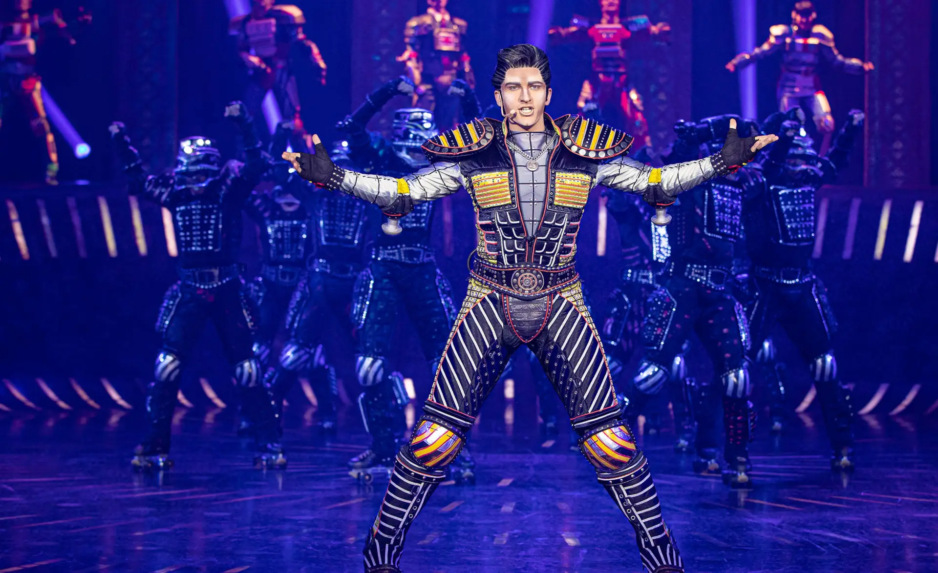Greaseball von Starlight Express steht im Vordergrund und breitet die Arme aus. Im Hintergrund stehen Tänzer.