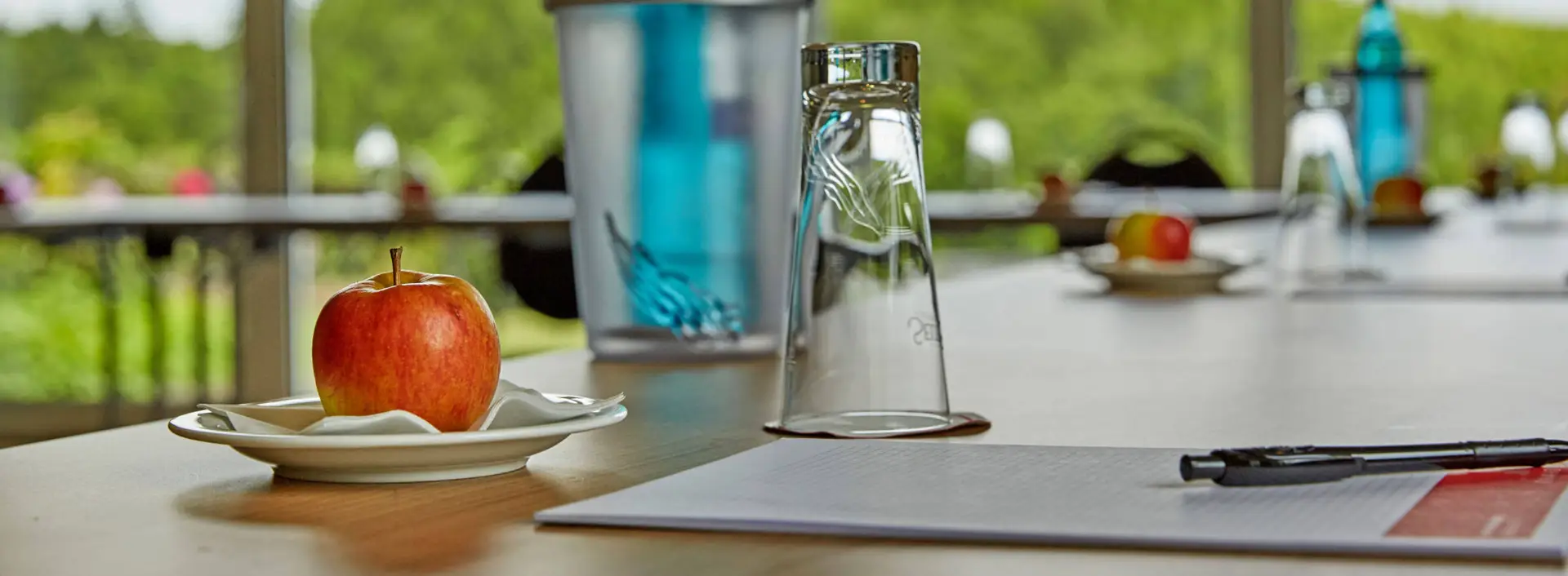 Nahaufnahme von einem Konferenztisch mit einem Apfel, eine Flasche Wasser und einem Schreibblock.