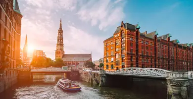 Speicherstadt mit Backsteinhäusern und im Hintergrund die St. Michaelis Kirche bim Sonnenaufgang. Auf der Elbe fährt eine Fähre.