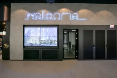Vier große Fernseher nebeneinander in der Lobby. An der Wand hängt oben mit Neonröhren geschrieben "Welcome".