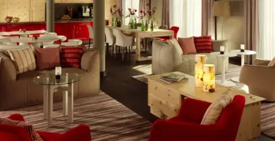 Große Lounge mit mehreren braunen Sofas und roten Stühlen. Im Raum stehen Holzmöbel und kleine Tische.