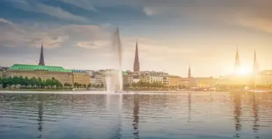 Skyline an der Hamburger Alster während des Sonnenuntergangs. Auf dem Wasser ist eine große Wasserfontäne.