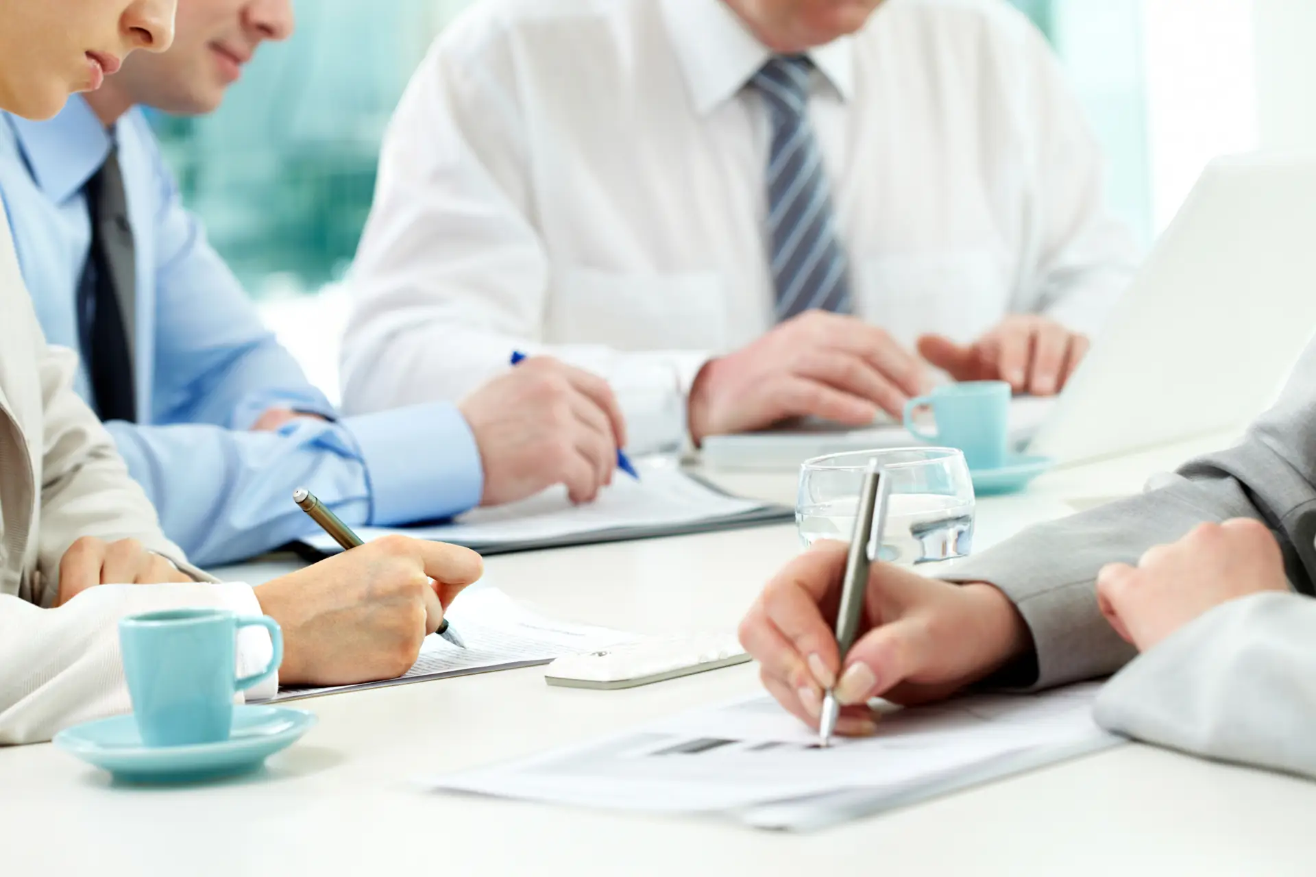 Vier Menschen im Businessoutift sitzen an einem Tisch und schreiben etwas auf Dokumenten.