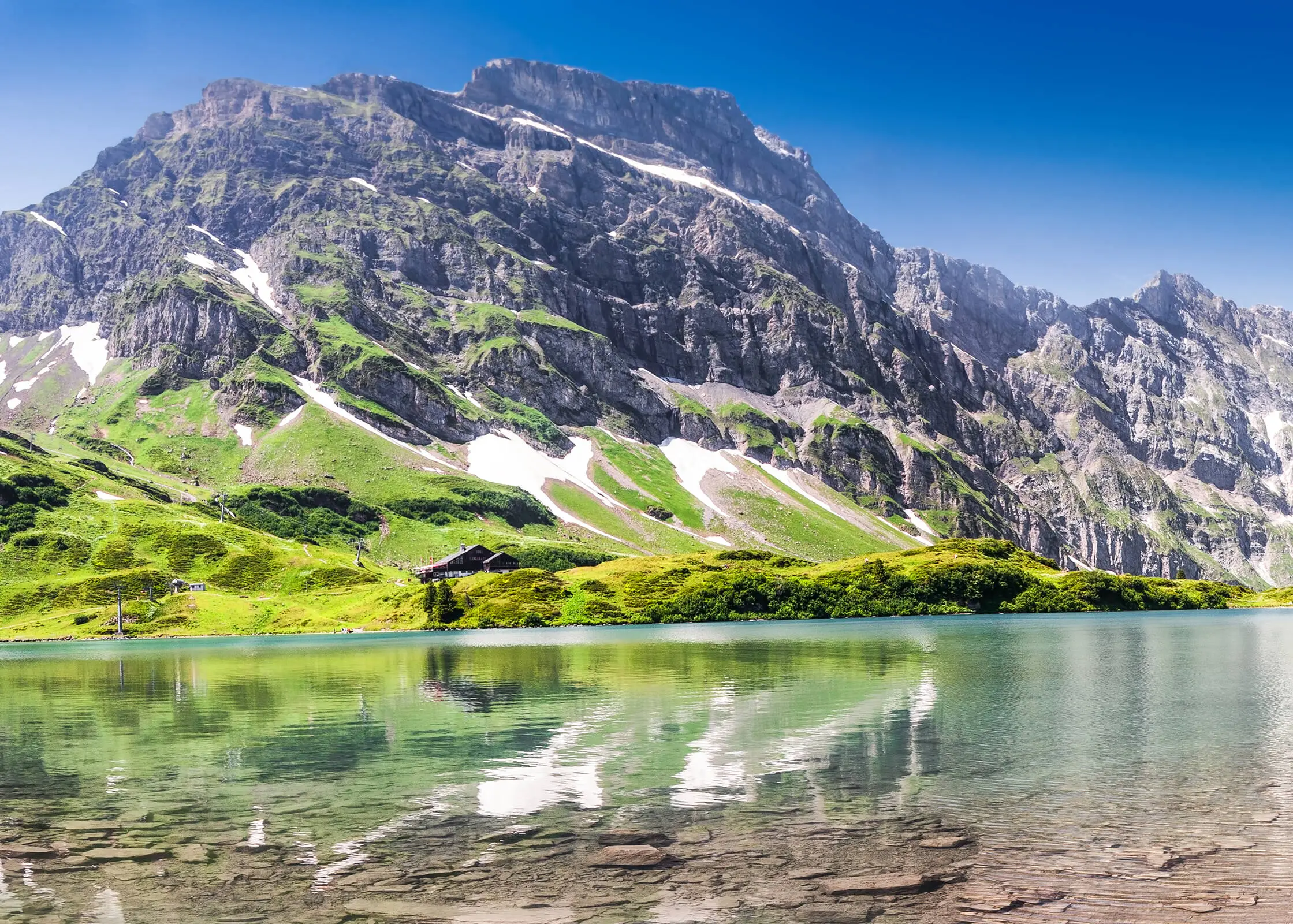 Blick über eine ruhigen Bergsee auf den Berg Titlis unter wolkenfreiem Himmel.
