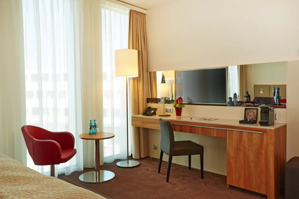 Schreibtisch mit einem kleinen Schrank und einem Fernseher an der Wand. Neben dem Schreibtisch steht eine Lampe und ein kleiner Tisch.