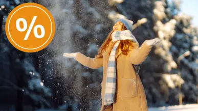 A woman in winter clothing stands outside and throws snow into the air.