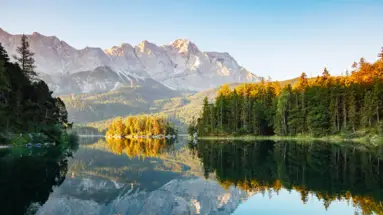 Gebirge und ein Nadelwald an einem glasklaren See.