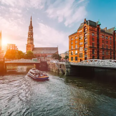 Hamburger Speicherstadt bei Tag mit einem Schiff auf dem Kanal. Im Hintergrund steht der Michel.