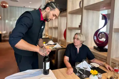 Nick Kobr präsentiert und öffnet den Wein der Ausbildungsverodnung gemäß am Tisch für Judith-Barbara Hindemitt Nick Kobr präsentiert und öffnet den Wein der Ausbildungsverodnung gemäß am Tisch für Judith-Barbara Hindemitt