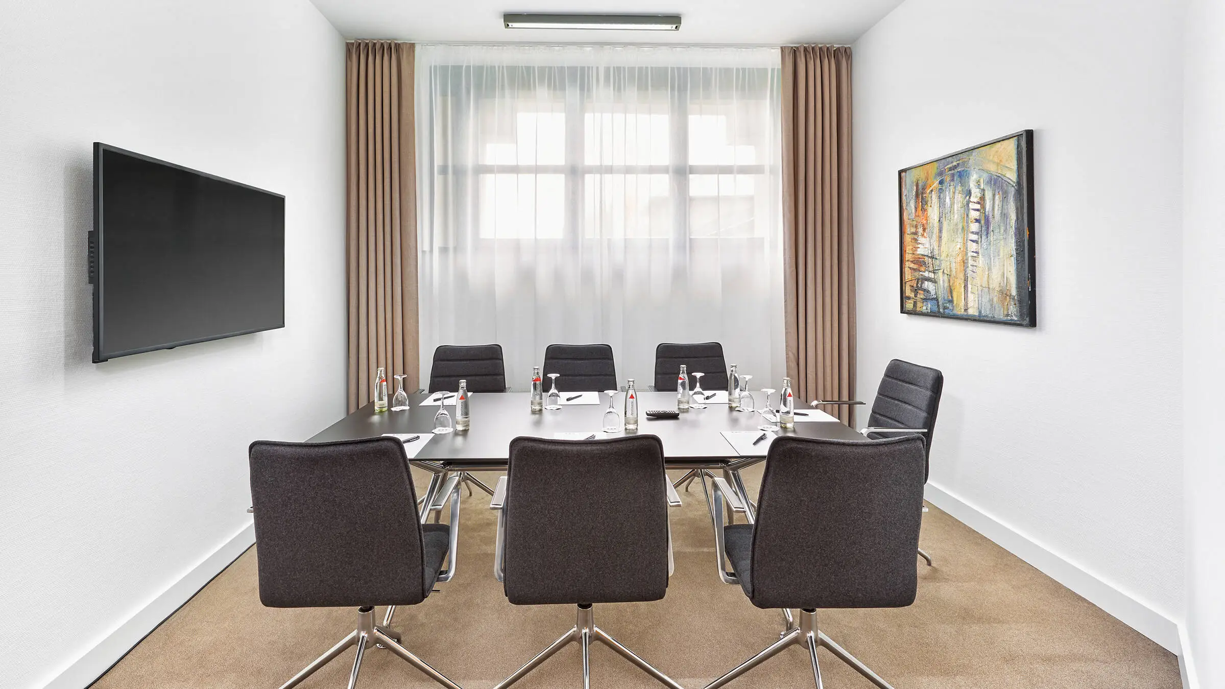 Kleiner Konferenzraum mit einem Konferenztisch. An der Wand hängt ein Fernseher.
