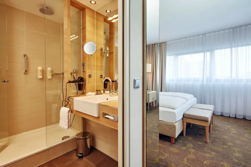 Badezimmer mit einer Dusche und einem kleinen Waschtisch. Auf der rechten Seite steht das Bett.