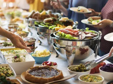 Buffet mit verschiedenen Speiseangeboten. Mehrere Menschen nehmen sich etwas davon.