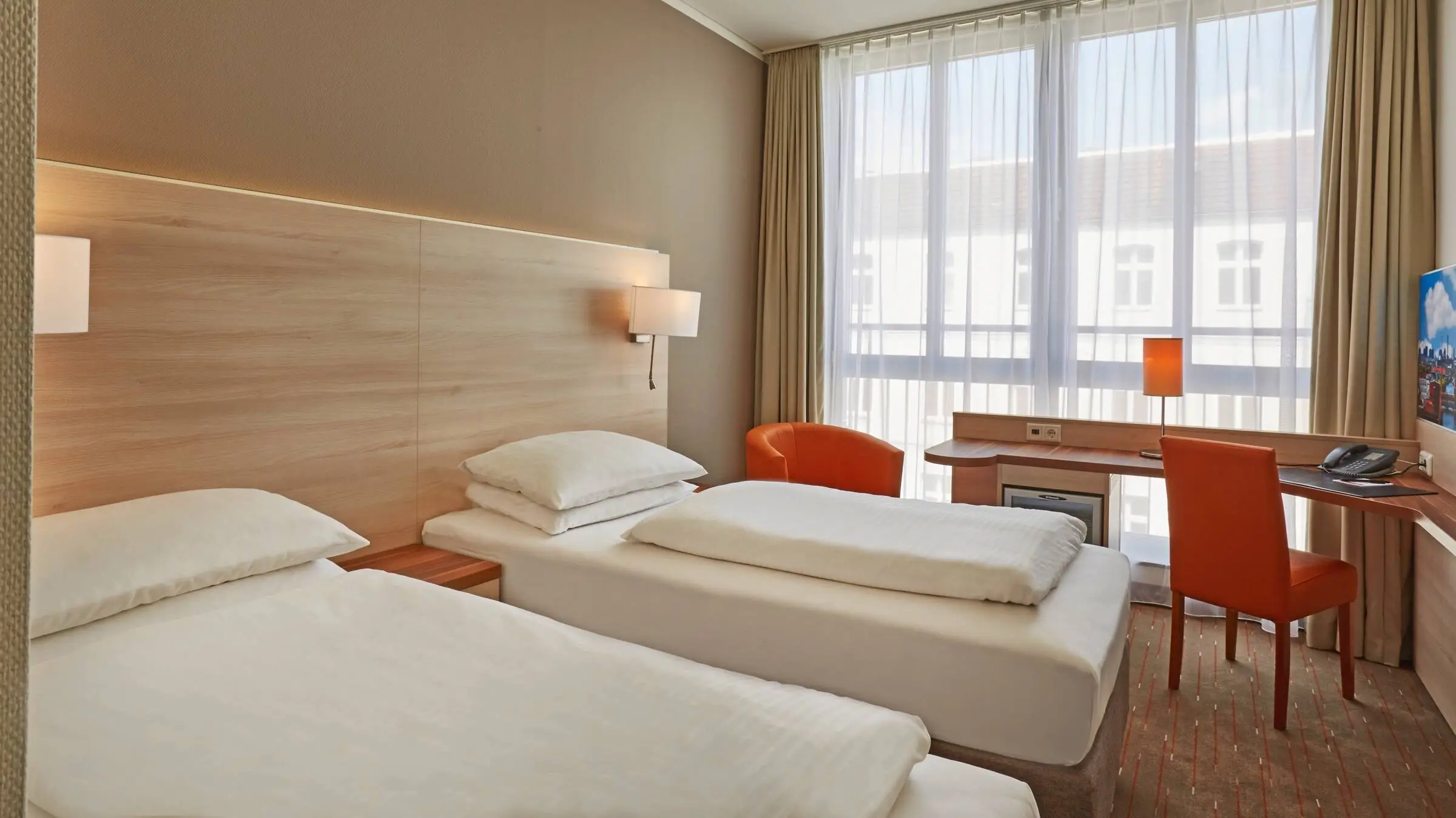 Twinbetten im Hotelzimmer. Vor dem Fenster steht ein Schreibtisch.