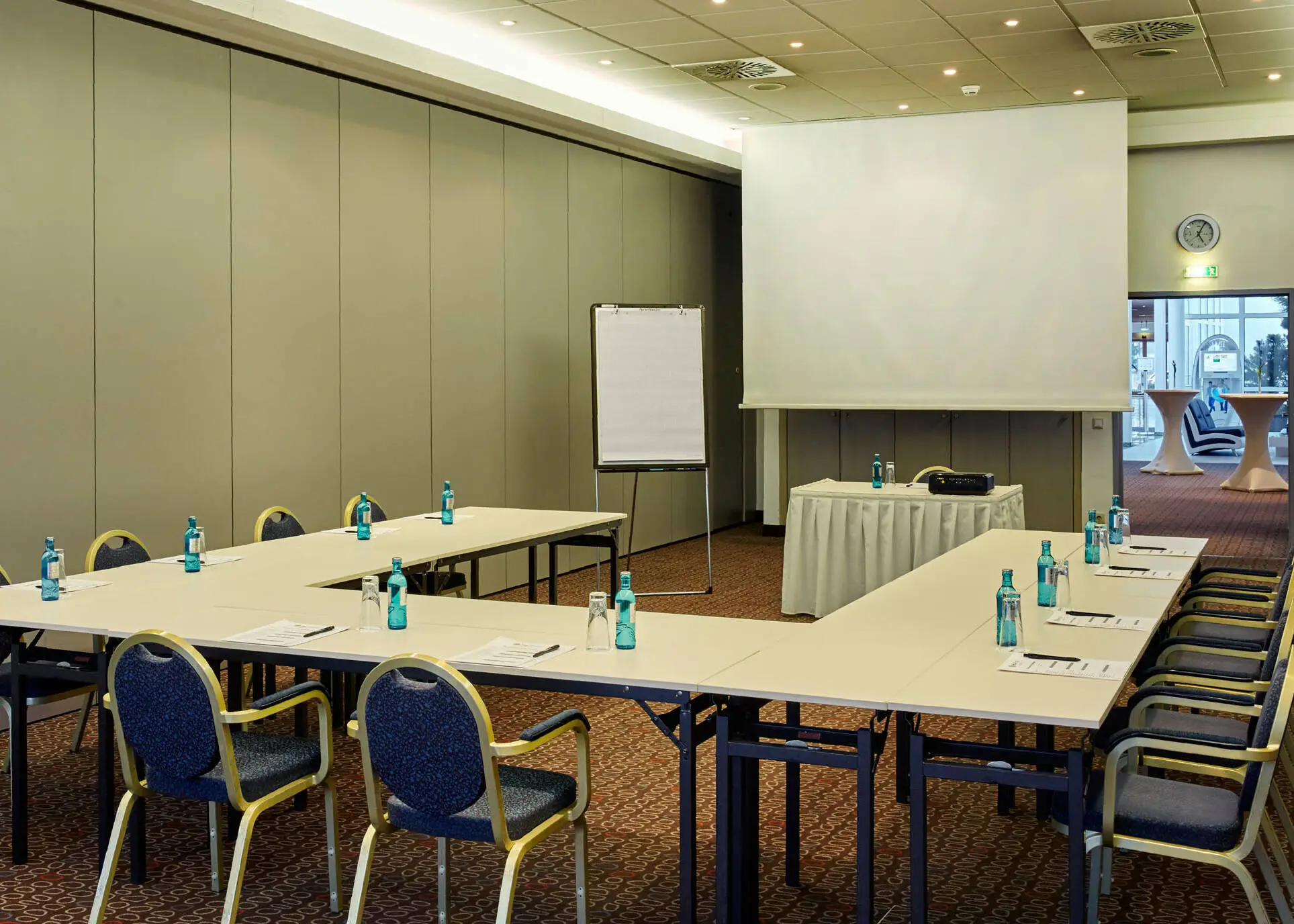Tagungsraum mit UForm Bestuhlung. In der Mitte steht ein Rednertisch mit einer großen Leinwand.