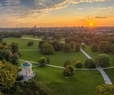 Blick von oben auf den Park und die Stadt beim Sonnenuntergang. Im Vordergrund steht ein Steinpavilion.