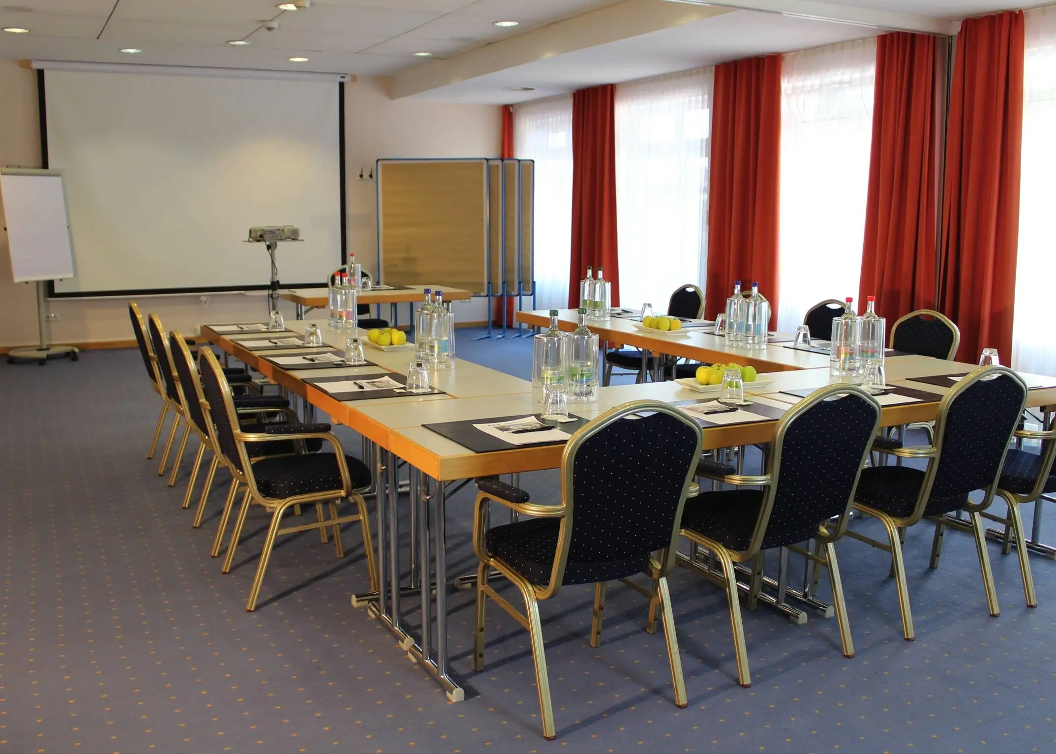 Konferenzraum mit einer UForm Bestuhlung. Hinter dem Rednertisch steht eine große Leinwand und eine Flipchart.