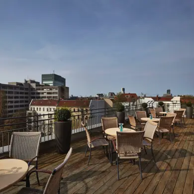 Dachterrasse mit Terrassenstühlen und Tischen. Im Hintergrund ist die Skyline von Berlin.