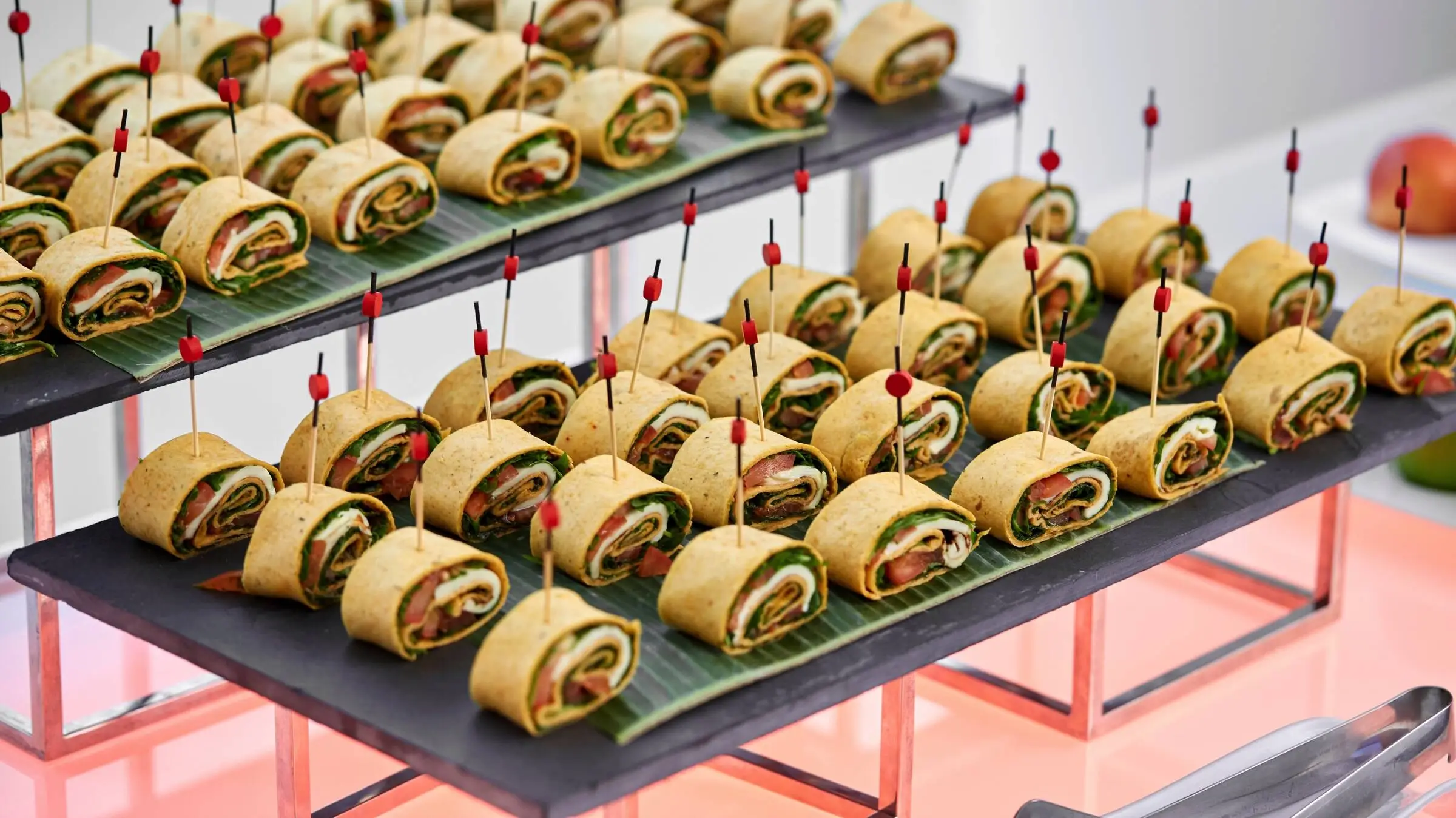 Detailaufnahme von zwei Schieferplatten auf denen gefüllte Eierkuchenrollen als Häppchen liegen. Detailaufnahme von zwei Schieferplatten auf denen gefüllte Eierkuchenrollen als Häppchen liegen.