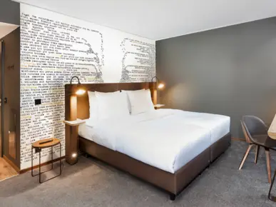 Doppelbett vor einer Wand mit in sich zusammenfallenden Wörtern an der Wand. 