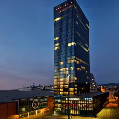 Torre de exposiciones con el Hyperion Hotel Basel iluminado por la noche